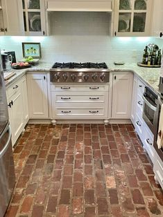 a kitchen with white cabinets and red brick flooring, including stainless steel stove top oven