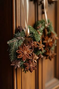 two wreaths are hanging on the front door with pine cones and evergreen leaves attached to them