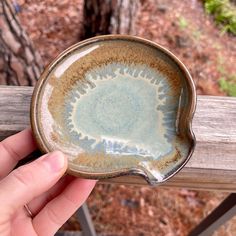 a hand holding a brown and blue dish on top of a wooden rail in the woods