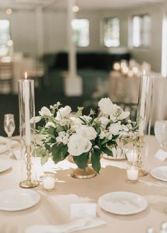 a table with white flowers and candles in vases on it's centerpiece