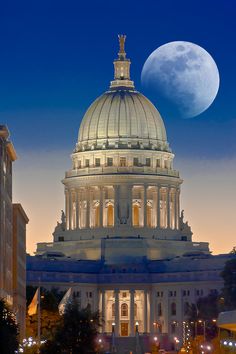 the capitol building is lit up at night with the moon in the sky above it