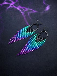 two pairs of beaded earrings are shown on a black surface with purple and blue lights