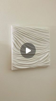 a white piece of art hanging on the side of a wall with a video play button