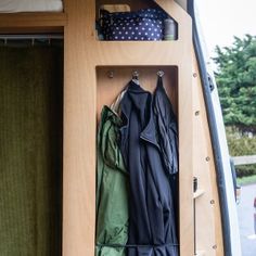 an open storage compartment in the back of a van with clothes hanging on hooks and pants