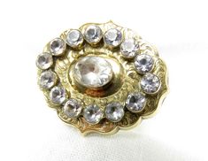 Circa 1820. This stunning Georgian 14KT yellow gold brooch with hand scroll design is centered by a beautiful oval colorless paste stone that measures 6.45mm x 7.60mm. Bezel set around the center stone are fourteen round paste stones that measures 4.70mm in diameter. This antique brooch is handmade. The Brooch measures38.75mm x 32.19mm x 7.40mm Appraised Value: $4,500 and is accompanied by an independent written appraisal. Heirloom Oval Gemstone Brooches, Oval Yellow Gold Brooches With Gemstone, Antique Oval Gemstone Brooch, Antique Gold Brooch With Gemstone, Antique Gold Gemstone Brooch, Antique Oval Gemstone Brooches, Antique Gold Jewelry With Center Stone, Heirloom Oval Brooch For Formal Occasions, Ornate Oval Engraved Brooches