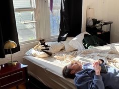 a man laying on top of a bed next to a window