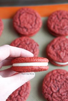 a person holding a red cookie in front of some cookies on a baking sheet with white frosting