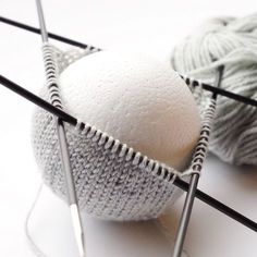 two balls of yarn sitting on top of knitting needles next to each other, one white and the other gray