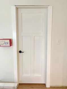 an empty room with a white door and wood flooring on one side and a red box on the other