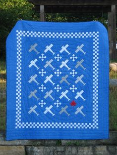 a blue quilt with airplanes on it in front of a wooden structure and grass area