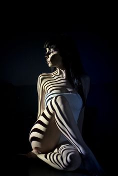 a woman sitting in the dark with stripes on her body