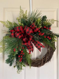 a wreath hanging on the front door with red and black plaid bow, evergreen leaves, berries and pine cones