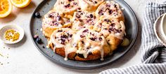 a blueberry scones with icing on a plate next to an orange slice