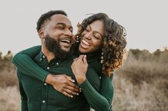 a man and woman smile as they hold each other in the middle of a field