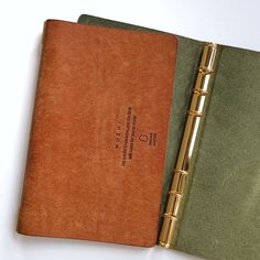 two notebooks sitting next to each other on top of a white table with a pen