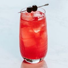 a red drink in a tall glass with a black cherry on the top and a silver straw sticking out of it