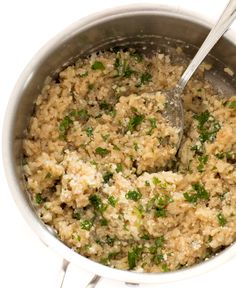 a large pot filled with rice and green onions next to a wooden spoon in it