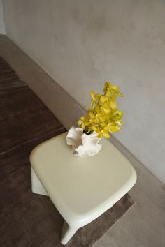 a white table with yellow flowers in it on the floor next to a gray wall