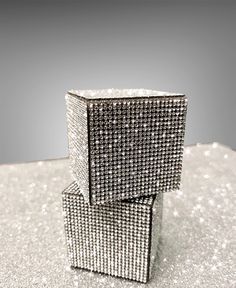 two silver boxes sitting on top of a table covered in glittery material, with one box open and the other closed