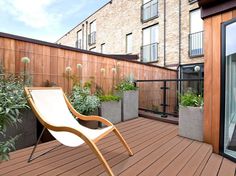 a wooden deck with a white chair and potted plants on the other side of it