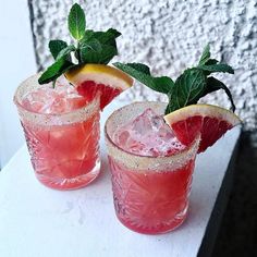 two glasses filled with pink lemonade and mint garnish on a white table