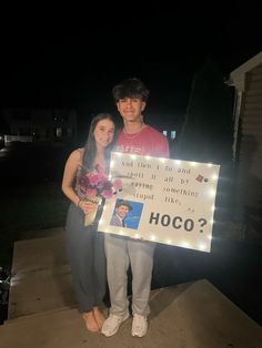 a man and woman standing next to each other holding a sign that says hoco?