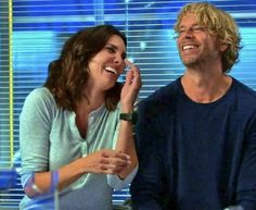 a man and woman sitting next to each other in front of a window talking on the phone