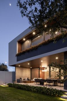 an exterior view of a modern house at night with lights on the windows and lawn area