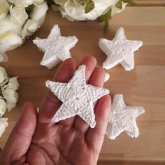 someone is holding some white crocheted stars in their hand, with flowers behind them