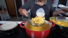 a woman stirring food in a red pot on top of a stove next to other cooking utensils