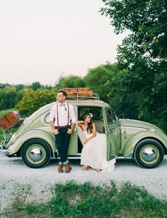 a bride and groom pose in front of an old beetle