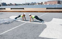 two women are doing push ups in an empty parking lot by the water on their skateboards