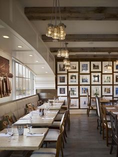 an empty restaurant with wooden tables and hanging pictures on the wall behind them, along with white linen covered booths