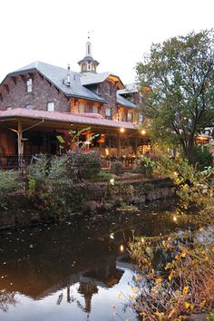 a large house sitting on top of a lush green hillside next to a river filled with lots of trees