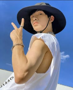 a young man wearing a black hat making the peace sign with his hand while standing in front of a blue sky