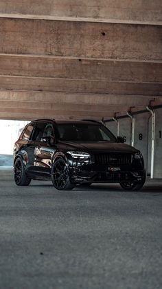 a black suv parked in an empty parking garage next to another car on the street