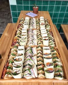 a long wooden tray filled with lots of sandwiches on top of a table next to a potted plant