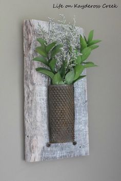 a metal vase with flowers in it hanging on a wall next to a wooden frame