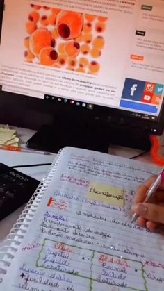 someone is writing on a notebook in front of a computer screen