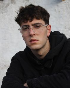 a young man wearing glasses sitting in front of a snow covered wall with his arms crossed