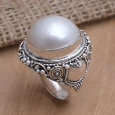 A large smooth pearl glows at the center of Nyoman Suka's ethereal cocktail ring. The Indian artisan hand crafts the ring's band from sterling silver accenting the precious metal with engraved braids and spirals and a pretty dot motif. A cultured Mabe pearl finishes the ring with incredible luster. Silver Pearl Ring With Cabochon, Heirloom Silver Oval Pearl Ring, Unique Silver Oval Pearl Ring, Artisan White Ring For Wedding, Unique White Oval Pearl Ring, Unique Oval White Pearl Ring, Silver Cabochon Pearl Ring For Gifting, Vintage Adjustable Silver Pearl Ring, Adjustable Vintage Silver Pearl Ring