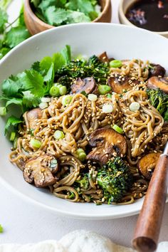 a white bowl filled with noodles, broccoli and mushrooms