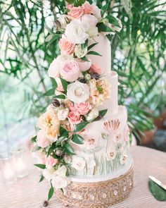 a wedding cake with pink and white flowers on the top is surrounded by greenery