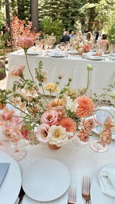 the table is set with white plates, silverware and pink flowers in vases