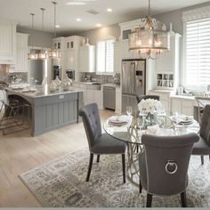 a dining room table and chairs in front of a kitchen with white cabinets, silver appliances and chandelier