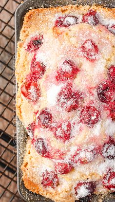 a cake with powdered sugar and cherries on it sitting on a cooling rack