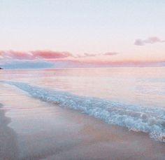 a beach with waves coming in to shore and the sun setting on the horizon behind it