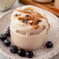 a dessert with blueberries and whipped cream on a white plate next to a wooden spoon