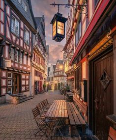 an empty wooden bench sitting in the middle of a cobblestone street next to tall buildings