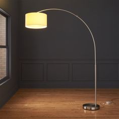 a floor lamp with a white shade on it in an empty room next to a window